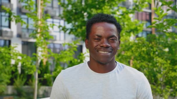 De cerca sonriente hombre afro-americano mira la cámara en el edificio moderno de fondo - Metraje, vídeo