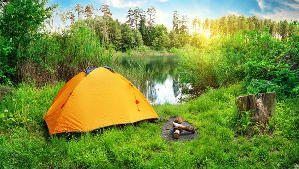 Pomarańczowy namiot na brzegu rzeki wśród zielonej trawy i drzew - Zdjęcie, obraz