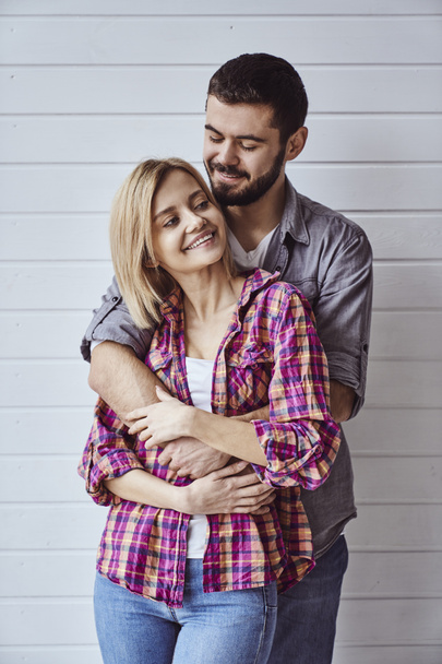 Portrait of young cheerful loving couple smiling looking at camera and hugging each other on light background - Foto, Imagem