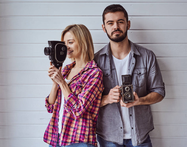Mladý šťastný pár při natáčení se starým fotoaparátem na světlém pozadí - Fotografie, Obrázek