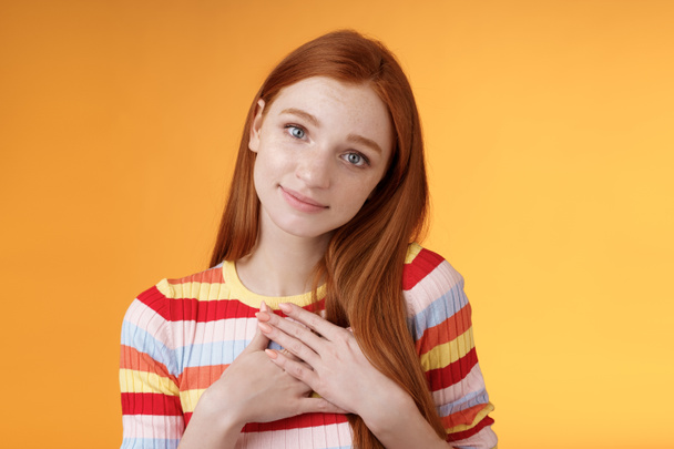 Lovely silly cute redhead young european girl tilting head look gently smiling tender camera press palms heart thankful receive nice gift gazing gratitude happiness, standing orange background - Foto, imagen
