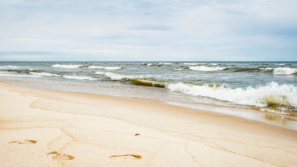 Ondas de mar e pegadas na areia na praia e céu nublado - Foto, Imagem