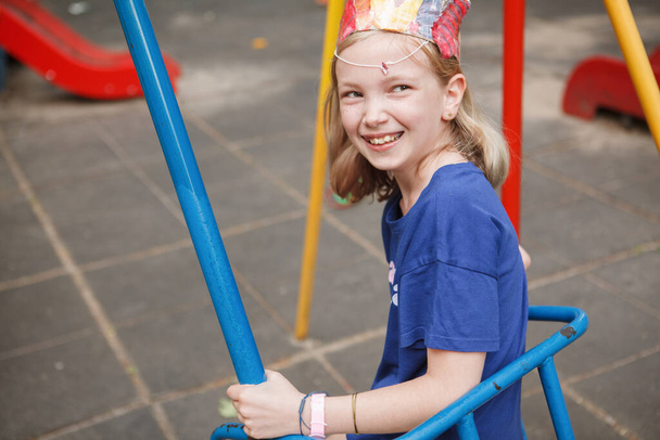 Happy young girl laughing joyfully, sitting on a swing on playground - Photo, Image