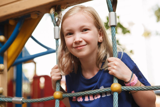 Gros plan d'une jeune fille joyeuse qui s'amuse à escalader un filet de corde sur une aire de jeux - Photo, image