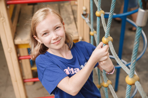 Close up de uma linda menina sorrindo, escalando corda net no parque infantil - Foto, Imagem