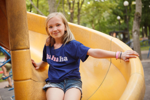 Menina feliz encantador deslizando em slide playground, sorrindo para a câmera - Foto, Imagem