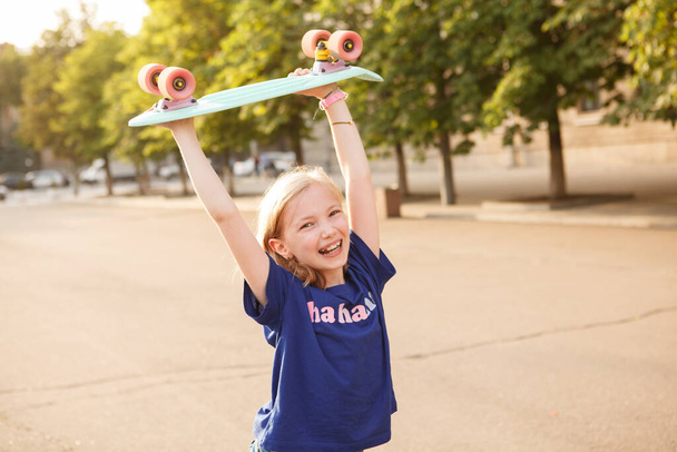 Happy young girl laughing, holding up her pennyboard in the air - Photo, Image