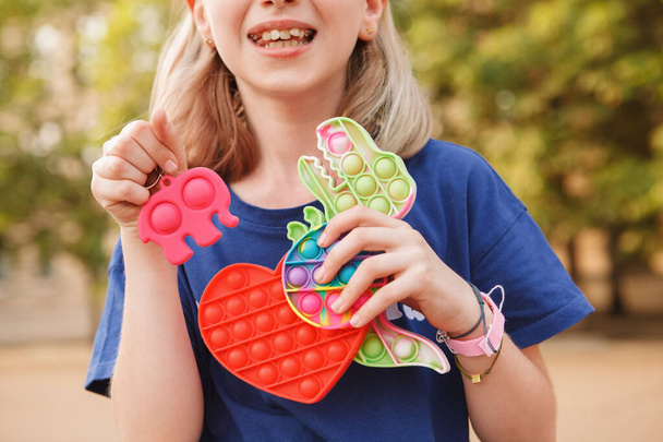Recortado cerca de una chica joven sonriendo, sosteniendo muchos juguetes coloridos pop it fidget - Foto, imagen
