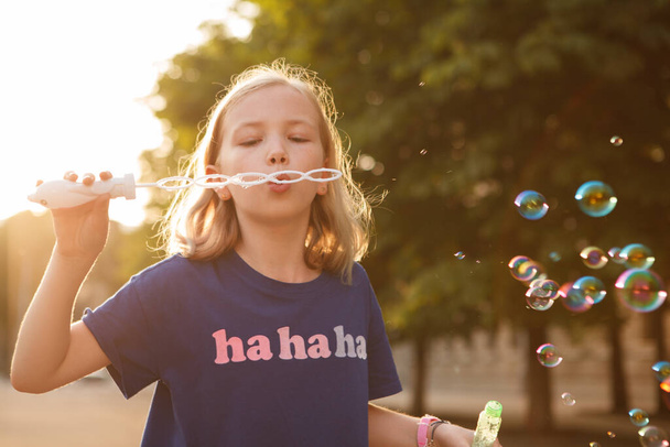 Blond haired young girl blowing bubbles outdoors in summer - Photo, Image