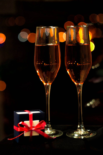 dwa kieliszki różowego szampana z pudełkiem na biżuterię na tle świateł nocnego miasta - Zdjęcie, obraz