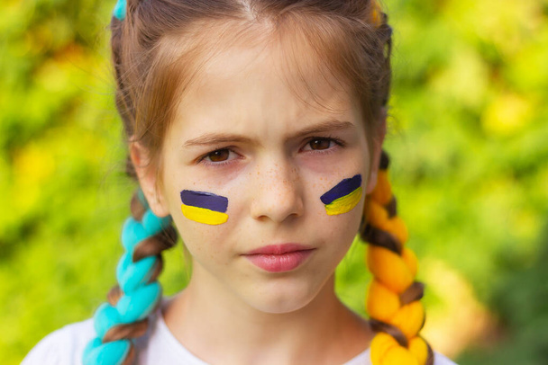 das Gesicht eines Mädchens mit gelb-blauen ukrainischen Nationalflaggen auf ihren Wangen. Konzept des ukrainischen Patriotismus, Unabhängigkeitstag. Unterstützung für Sport und Fans. - Foto, Bild