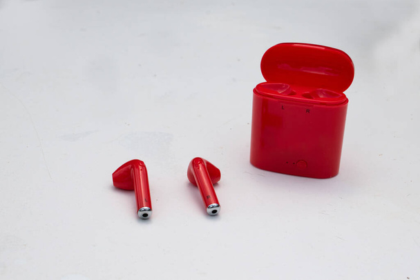 Un par de auriculares o auriculares inalámbricos de color rojo brillante aislados sobre un fondo gris con una caja de carga. - Foto, Imagen