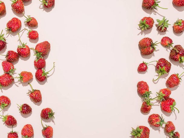 Erdbeeren mit Stecklingen ergeben ein Muster. Die Beeren befinden sich an den Seiten, chaotisch. Blick von oben. Pudriger Hintergrund. Flach lag er. Sommermuster. Hartes Licht. Helle Schatten. Kopierraum. - Foto, Bild