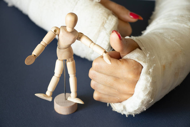 dvě ženské ruce se zlomenými zápěstími po pádu z kola v sádře na izolovaném pozadí s dřevěnou figurínou muže, ruce v sádře - Fotografie, Obrázek