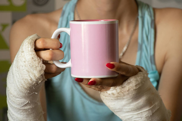dívka se dvěma zlomenými pažemi v sádře drží šálek čaje v kuchyni k snídani, zlomené paže v sádře, zlomené končetiny, zranění - Fotografie, Obrázek