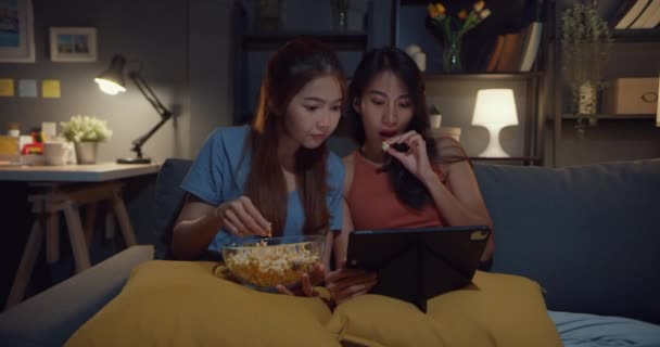 Keyifli anın tadını çıkaran Asyalı çekici hanımlar tablet üzerinde online film eğlencesi izleyin geceleri evdeki kanepe oturma odasında patlamış mısır yiyin. Yaşam tarzı aktivite karantina konsepti. - Video, Çekim