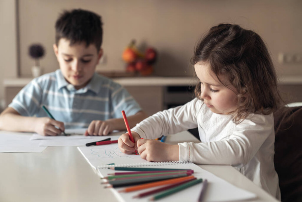 Fratellino e sorella felici seduti a un tavolo in cucina e disegnare un quadro con matite colorate e pennarelli - Foto, immagini
