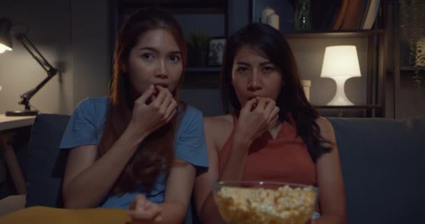 Attraktive asiatische Paar Damen empfinden Schock und Angst Moment essen Popcorn sehen Horror Online-Film Unterhaltung auf dem Sofa im Wohnzimmer zu Hause dunkle Nacht. Konzept der Quarantäne für Lebensstil am Wochenende. - Filmmaterial, Video