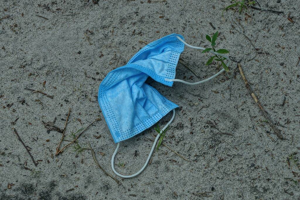 garbage from one blue dirty medical mask lies on gray sand in the street - Photo, Image