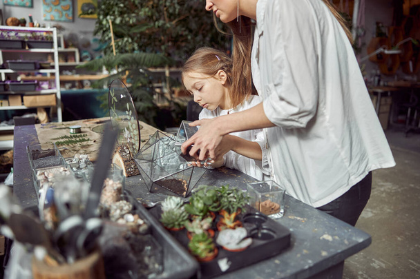 Кавказский уверенный в себе счастливый флорист работает со своей маленькой дочерью и создает композицию из стеклянных камней и растений в ботаническом цехе - Фото, изображение