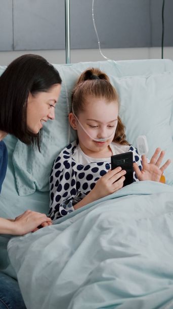 Mother and sick daughter greeting friends having online videocall telecommunication - 写真・画像