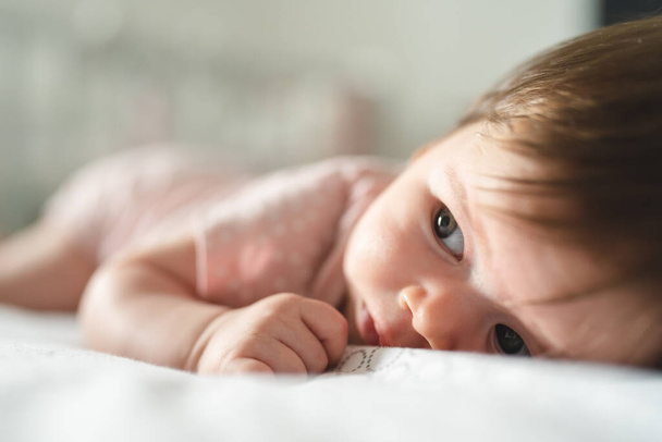 Nahaufnahme des kleinen kaukasischen Babys von vier Monaten, das zu Hause auf dem Bett in einem hellen Raum mit Kopierraum liegt - Foto, Bild