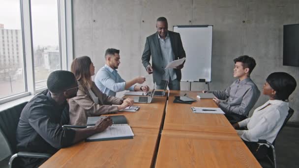 Afrikai érett férfi vezető mentor vezető edző áll irodai tanácsteremben, hogy kollégák multiraciális üzleti csapat papír dokumentumok másolata szerződés információs adatok utasítás személyzet képzés - Felvétel, videó