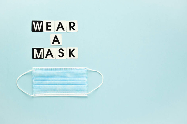 One medical mask and a text message wear a mask on a light blue background. Poster, banner virus protection. An empty space. - Photo, image