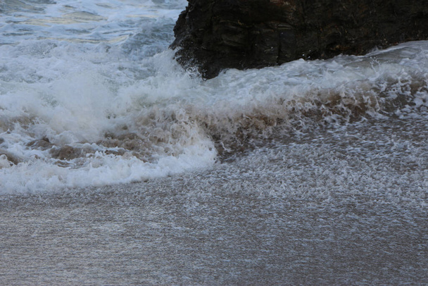 Atlantik fırtınası dalgaları İngiltere 'nin güney batı kıyısındaki Cornwall' daki Carlyon körfezi plajında kayaların ve kumların üzerine düşüyor. - Fotoğraf, Görsel