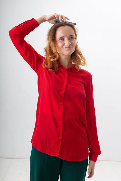 νεαρή Καυκάσια κοκκινομάλλα κοπέλα με κόκκινο πουκάμισο χαζολογάει με το κινητό τηλέφωνο - Φωτογραφία, εικόνα