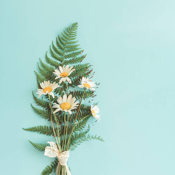 Cosy bouquet of rural chamomile flowers with fern on blue background with copy space. - Zdjęcie, obraz