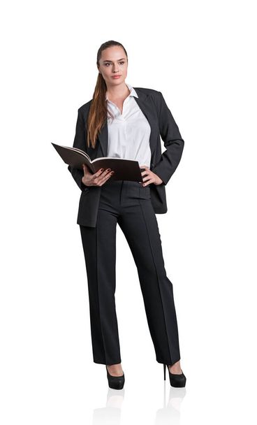 Attractive business woman in formal suit and high heels is holding a planner, notebook or her notes. Full length businesswoman Isolated over white background - Photo, image