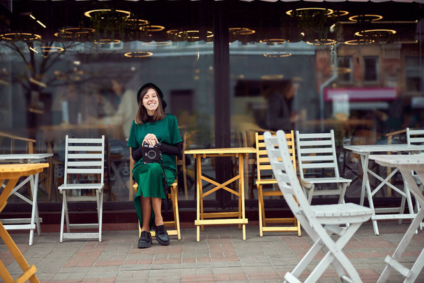 Happy woman in green dress in urban city is sitting near cafe - Photo, image
