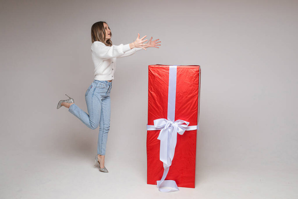 cheerful female model poses for the camera with a big red box with her christmas present and rejoices a lot - Photo, Image