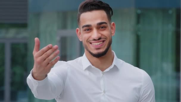 Portrait friendly smiling toothy hispanic arab business man spaniard boss wears white formal shirt showing gesture of invitation advice to approach with hand asks to come outdoors, body languages sign - Footage, Video