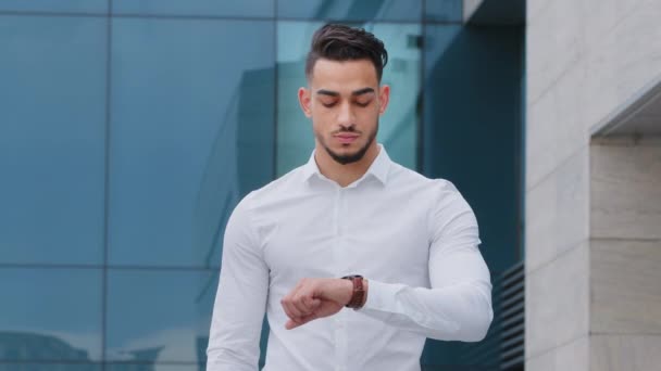 Portret ernstig overstuur ongeduldig latino man bebaarde man ontevreden zakenman draagt formele stijlvolle shirt staat buiten kijken naar pols horloge bezorgd over te laat zijn tijd rush wachten - Video