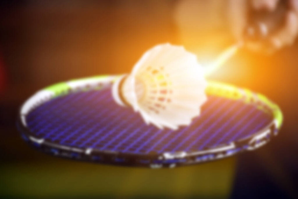 Blurred image of badminton racket and white badminton shuttlecock on badminton court. soft and selective focus on shuttlecock. - Photo, Image