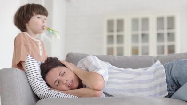 Zmęczona zestresowana matka nadpobudliwego dziecka leżącego na sofie wkurzona hałasem ze strony nieposłusznego małego syna - Materiał filmowy, wideo