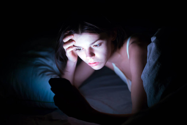  Egy álmatlanságban szenvedő nő videót néz a neten egy készüléken.. - Fotó, kép