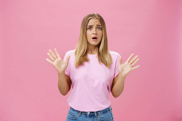 Woman looking nervous explaining with panicking gestures she not involved frowning opening mouth and gasping feeling concerned and worried waving hands over chest posing against pink wall - Photo, Image