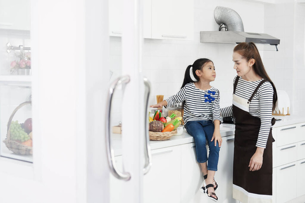 Uśmiechnięta azjatycka matka i mała azjatycka dziewczynka uczą się gotować razem w kuchni na wakacjach. Rodzina miłość i edukacja dla Homeschool Concept. - Zdjęcie, obraz