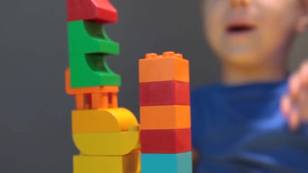 Een mooie jongen speelt thuis met bouwstenen. Een schattige lachende jongen speelt met een lego constructeur met veel kleurrijke plastic blokken in de kamer, het bouwen van een stad. Kleuterklassen. - Video
