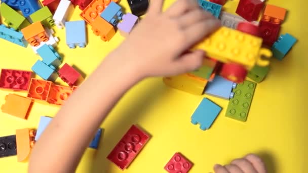Een mooie jongen speelt thuis met bouwstenen. Een schattige lachende jongen speelt met een lego constructeur met veel kleurrijke plastic blokken in de kamer, het bouwen van een stad. Kleuterklassen. - Video