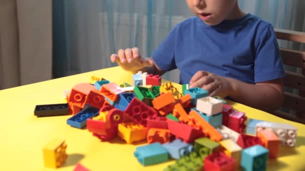 美しい男の子が家でブロックを作って遊んでいる。かわいい笑顔の男の子は、部屋の中にカラフルなプラスチックブロックがたくさんあるレゴのコンストラクタで遊んでいる、都市を建設しています。就学前. - 映像、動画
