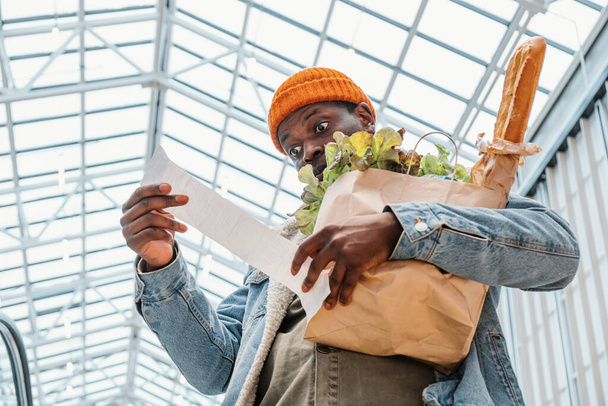 Sorpreso uomo nero guarda totale ricevuta con il cibo nel centro commerciale - Foto, immagini