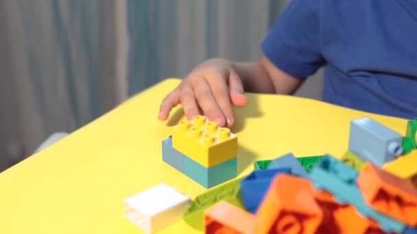 Un niño hermoso está jugando en casa con bloques de construcción. Un niño sonriente lindo está jugando con un constructor lego con un montón de bloques de plástico de colores en la habitación, la construcción de una ciudad. Clases preescolares. - Metraje, vídeo