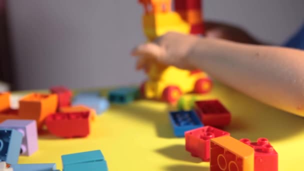 Un niño hermoso está jugando en casa con bloques de construcción. Un niño sonriente lindo está jugando con un constructor lego con un montón de bloques de plástico de colores en la habitación, la construcción de una ciudad. Clases preescolares. - Metraje, vídeo