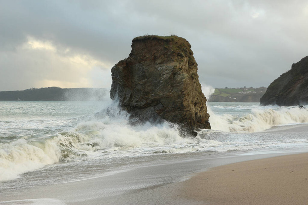 大西洋のどこか遠くの嵐によって打ち上げられ、イングランドの南西部のコーンウォールの海岸に墜落した強力な波によって推進されているカリヨン湾のビーチの岩の孤立した柱 - 写真・画像