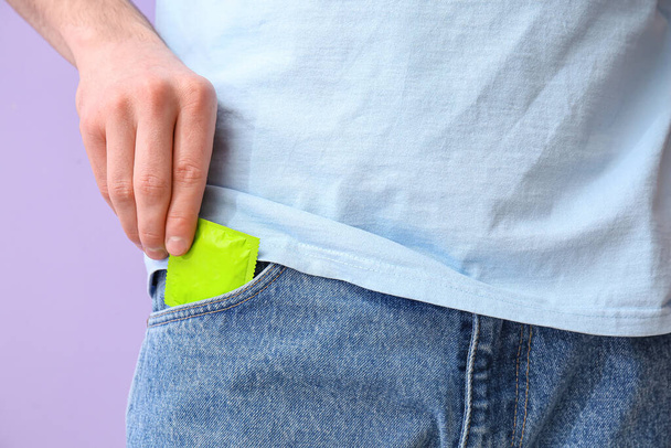 Άνθρωπος βάζοντας προφυλακτικό στην τσέπη του τζιν στο φόντο χρώμα, closeup - Φωτογραφία, εικόνα