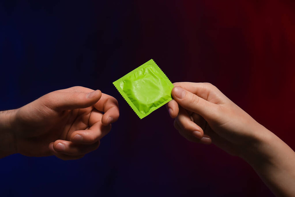 Hands of couple with condom on dark background - Photo, Image